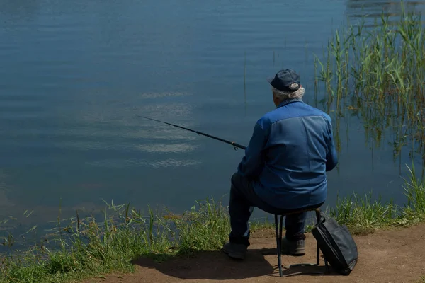 Рыбак с удочкой ловит рыбу, сидя на берегу реки . — стоковое фото
