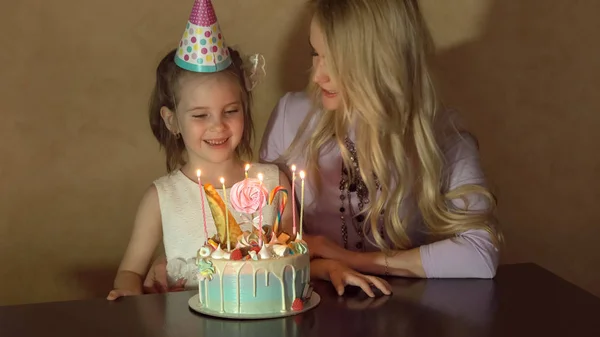 Madre e hija soplan velas en un pastel de cumpleaños y piden un deseo. el cumpleaños de una niña — Foto de Stock