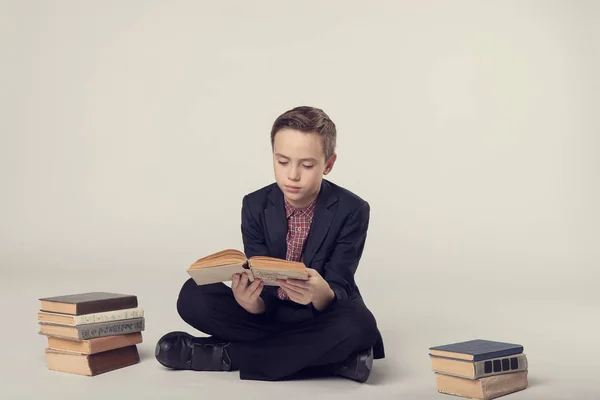 Carino ragazzo in un abito seduto e tenendo un libro su uno sfondo grigio — Foto Stock