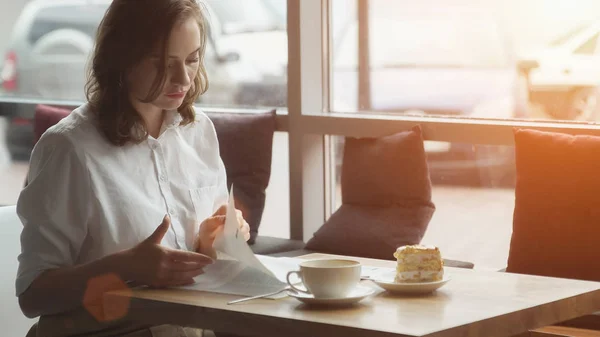 Atractiva joven pasa tiempo libre sentado en cafés, disfrutando del café fresco y leyendo una revista de mujeres —  Fotos de Stock