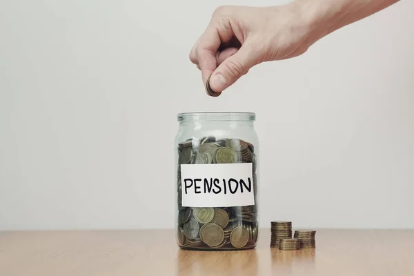 Distribuzione del concetto di risparmio in contanti. Mano mette monete alle casse di vetro con iscrizione 'pension' . — Foto Stock