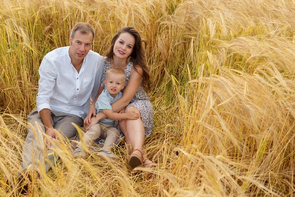 Familia feliz sentada en un trigo en el campo — Foto de Stock