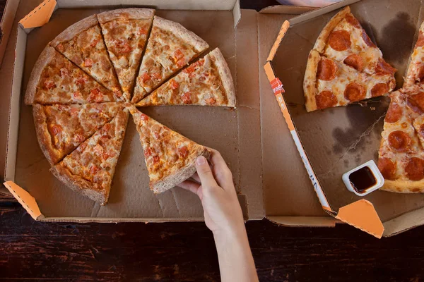 Fresh pizza in box and hand hold piece, top view — Stock Photo, Image