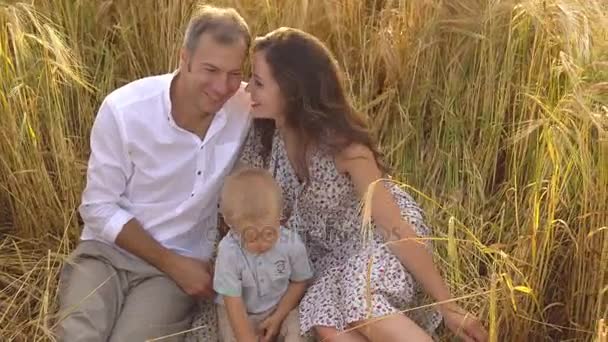 Feliz familia sonriente sentada en trigo en el campo — Vídeos de Stock