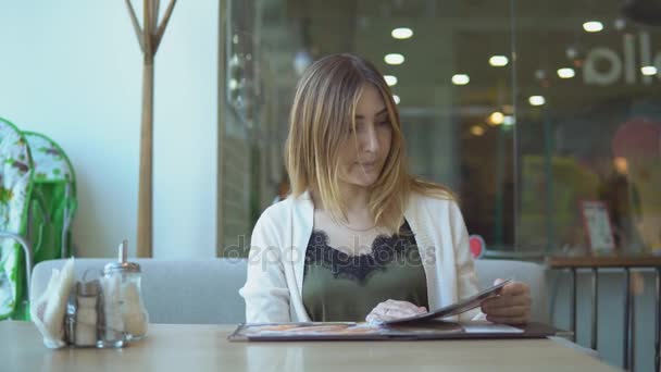 Young woman in a restaurant with the menu in hands and calling the waiter — Stock Video