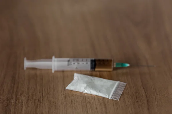 Paquet plastique avec poudre de cocaïne et seringue sur table en bois . — Photo