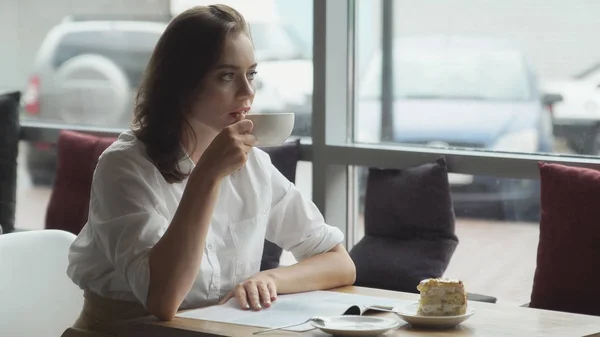 Attraktive junge Frau verbringt ihre Freizeit in Cafés, genießt den frischen Kaffee und liest eine Frauenzeitschrift — Stockfoto