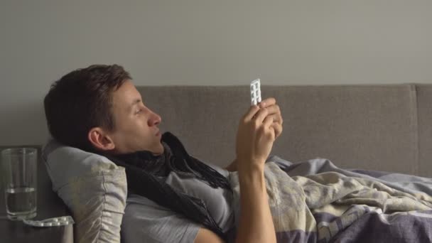 Chory człowiek leżąc w łóżku obok jego leki w jego domu i bierze lekarstwo — Wideo stockowe