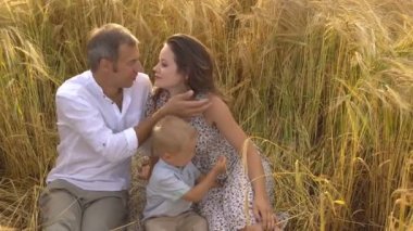 Bir buğday alanda çimlerin üzerine oturan aile