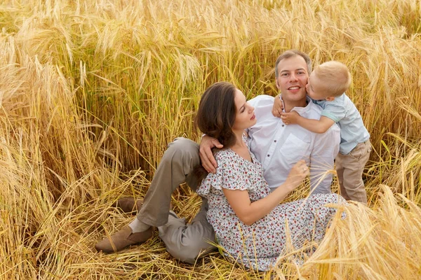 Familia sentada en la hierba en un campo de trigo — Foto de Stock