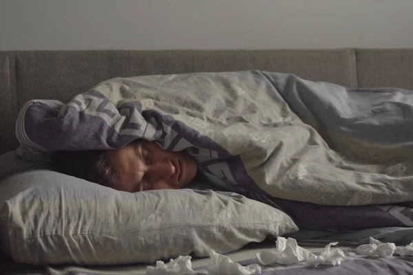 Больной молодой человек спит в постели, покрытый одеялом — стоковое фото