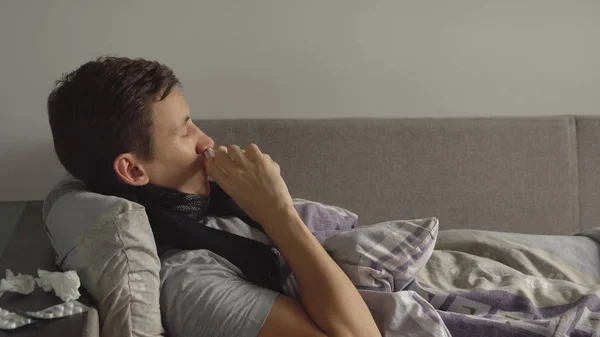 Hombre acostado enfermo en la cama junto a sus medicamentos en su casa y espolvorea un aerosol nasal en su nariz — Foto de Stock