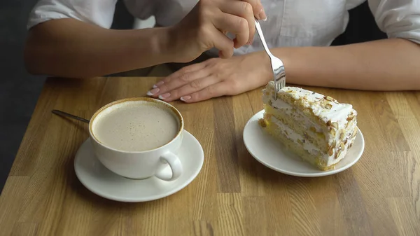 Una chica bebe café y come un pastel dulce en un café. Primeros planos de manos femeninas — Foto de Stock