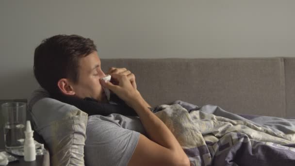 Hombre acostado enfermo en la cama junto a sus medicinas en su casa y sonándose la nariz en un pañuelo — Vídeos de Stock