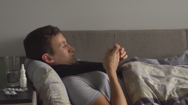 Nezdravé muž v posteli vedle jeho léky ve svém domě volání na telefonu. Muž trpí zima a zimní chřipkový virus — Stock video
