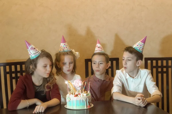 La pequeña cumpleañera y sus amigos para la mesa de vacaciones. los niños soplan velas en un pastel de cumpleaños. fiesta de cumpleaños de niños —  Fotos de Stock