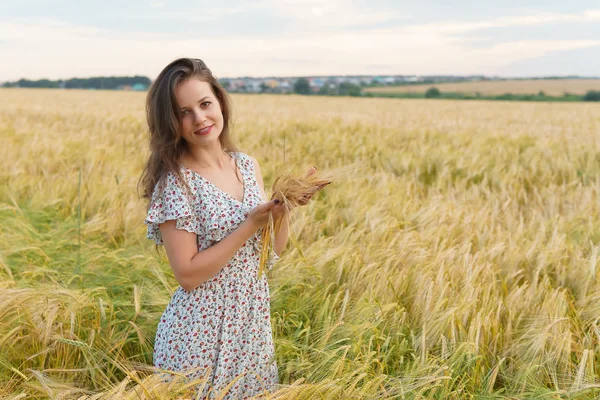 Mulher jovem no vestido mantém orelhas de trigo em mãos — Fotografia de Stock