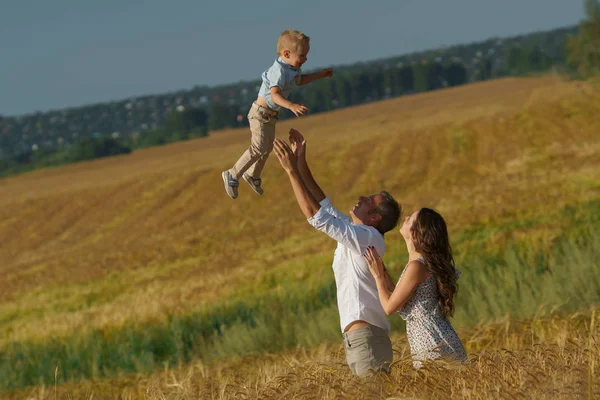 Jovens pais e criança caminhando pelo campo de trigo — Fotografia de Stock