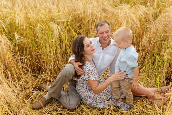Familia sentada en la hierba en un campo de trigo — Foto de Stock