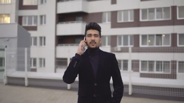 Retrato de atractivo hombre de negocios delgado en traje formal hablando en el teléfono inteligente contra el telón de fondo del centro de negocios — Vídeo de stock