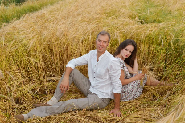 Casal feliz sentado na grama em um campo de trigo — Fotografia de Stock