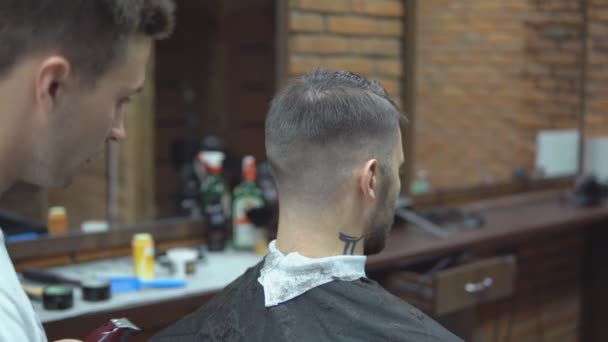 Мастер стрижет волосы и бороду мужчин в парикмахерской, парикмахер делает прическу для молодого человека — стоковое видео