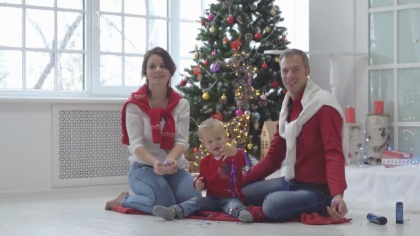 Lycklig familj med konfetti på bakgrund av julgran med gåvor. — Stockvideo