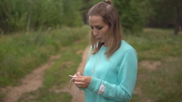 Beautiful young sports girl with phone breathes heavily after jogging. — Stock Video