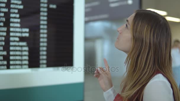 Красивая молодая женщина стоит рядом с табло с уведомлением и выбор номер рейса — стоковое видео