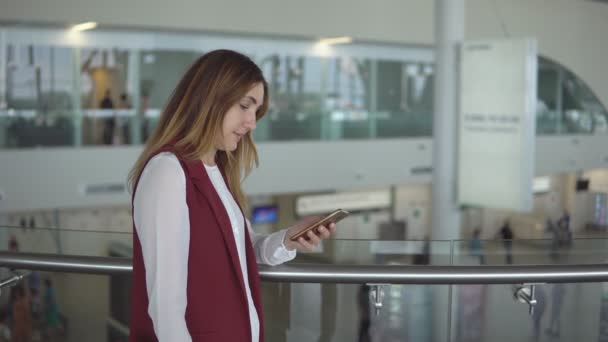 Junges Mädchen in eleganter Kleidung steht am Flughafen und tippt ins Smartphone. — Stockvideo