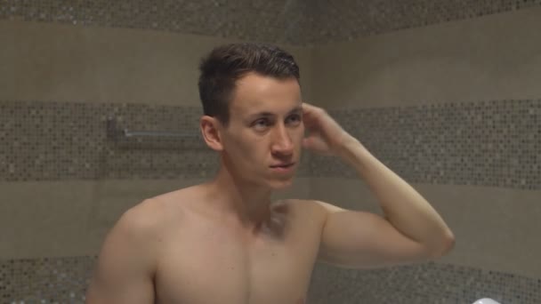 Young attractive man straightens hairstyle after a shower in the bathroom of the hotel room. — Stockvideo