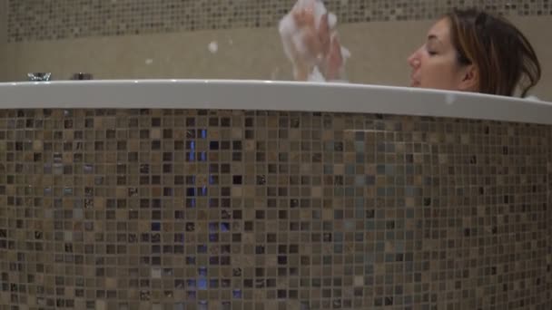 Mulher morena bonita tomando banho espumoso e brincando com espuma de sabão . — Vídeo de Stock