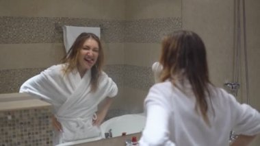 Sevimli kız beyaz bornoz dans ve şarkı söyler banyoda ayna önünde