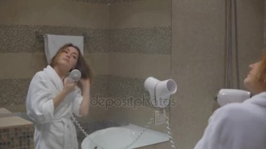 genç kız beyaz bornoz aynanın önünde banyoda saç kurutma makinesi ile saç kurur