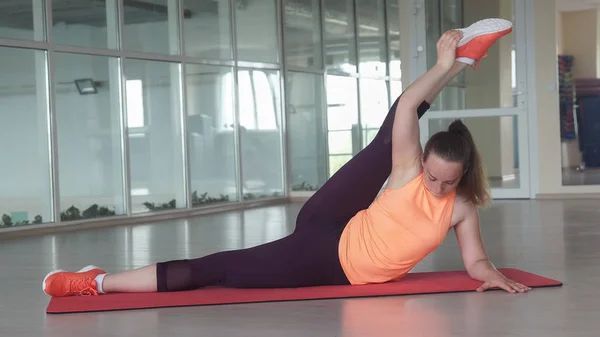 Joven mujer deportiva hace ejercicio de estiramiento difícil en la estera del gimnasio mientras entrena en el gimnasio — Foto de Stock