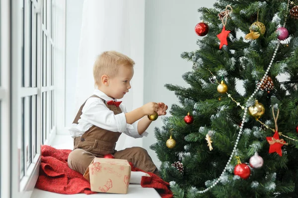 Der kleine Junge schmückt einen Weihnachtsbaum mit Spielzeug. Urlaub, Geschenk und Neujahrskonzept — Stockfoto