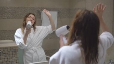 Sarışın kadın çekici saç kurutma makinesi ile şarkı söylüyor