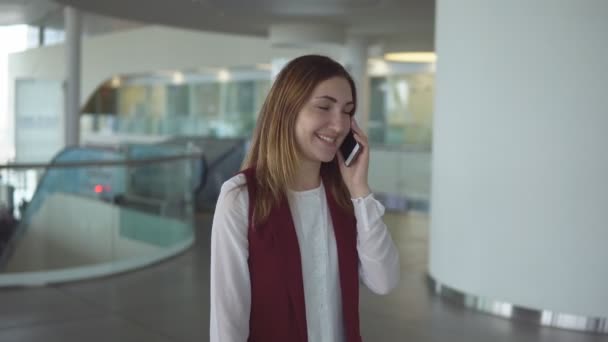 Chica joven positiva en ropa elegante habla en el teléfono inteligente en el aeropuerto . — Vídeo de stock