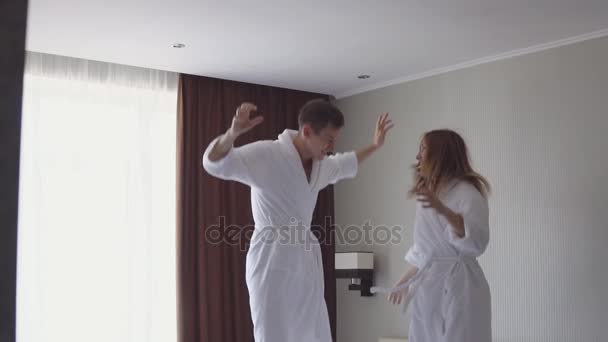 Zeitlupenvideo von jungen Paaren, die nach ihrer Ankunft im Hotel auf dem Bett springen und tanzen — Stockvideo