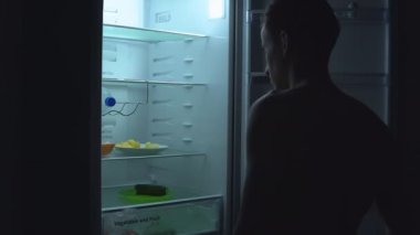 Aç adam gece buzdolabında yemek yiyecek arıyor.
