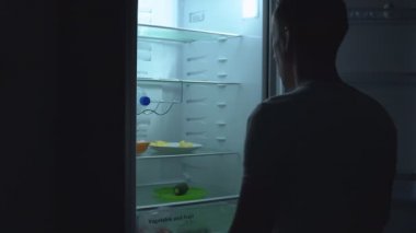 Aç adam gece buzdolabında yemek yiyecek arıyor.