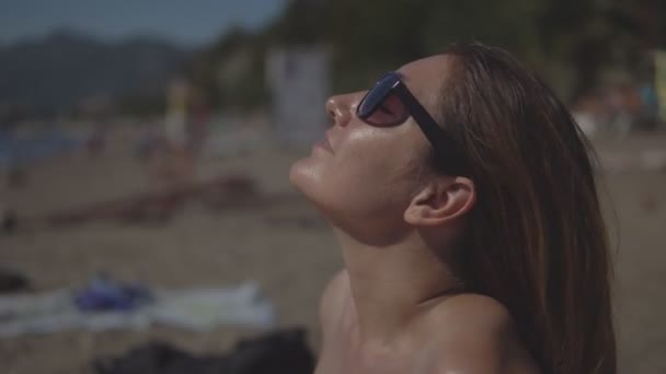 Красивая девушка в солнечных очках летом отдыхает и загорает на пляже — стоковое видео