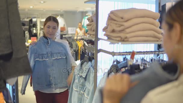 Mooi meisje kijkt naar haar reflectie in de spiegel terwijl proberen op kleding in mode tijdens het winkelen — Stockvideo