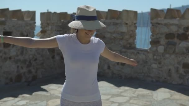 Leuke jonge vrouw in hoed draait en dwarrelen op de stenen fort op zonnige zomerdag — Stockvideo
