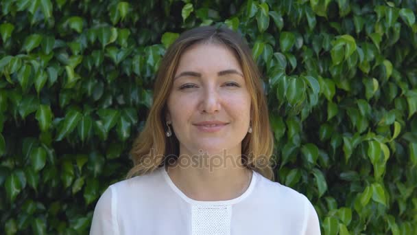 Belle femme d'affaires souriant sur fond de haie verte de buissons le jour ensoleillé — Video