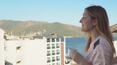 Oteldeki odasına balkonunda dururken kahve içme bornoz güzel genç kız.