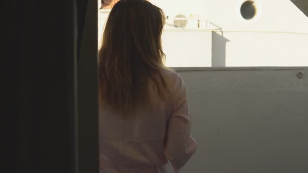 Belle fille en peignoir va sur le balcon de sa chambre à l'hôtel et profite du café . — Video