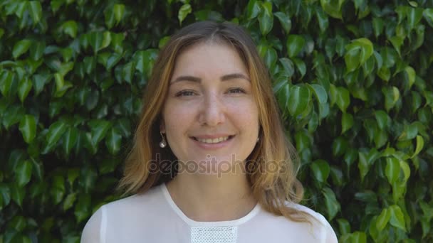 Hermosa mujer de negocios sonriendo en el fondo de cobertura verde de arbustos en el día soleado — Vídeos de Stock