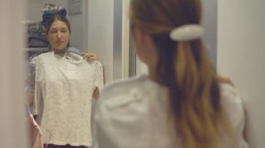 Güzel kız çalışırken giysi moda mağaza alışveriş yaparken yansıması Aynaya bakar.