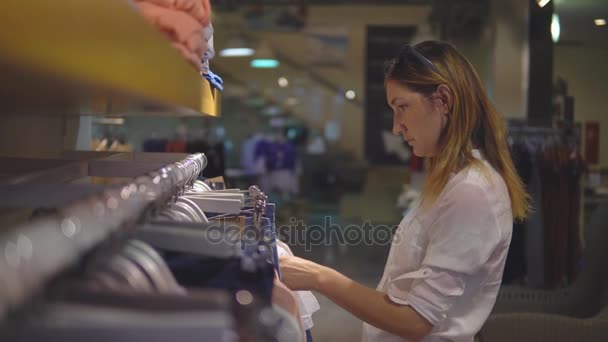 Roupa, guarda-roupa, moda, estilo e conceito de pessoas - mulher loira feliz escolhendo roupas na loja — Vídeo de Stock